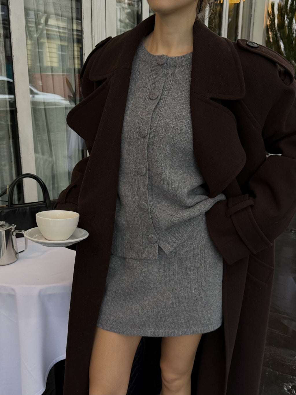 Жінка в коричневому максі пальто Muse тримає чашку кави, вид зблизька